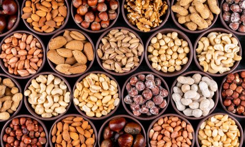 Set of pecan, pistachios, almond, peanut, cashew, pine nuts and lined up assorted nuts and dried fruits in a mini different bowls on a black stone background. flat lay.